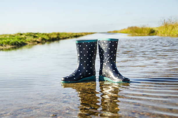 蓝色的孩子们的橡胶靴子上有白点，单独矗立在一条从海洋流出的水道上，这是斯堪的纳维亚自然的水道图片下载
