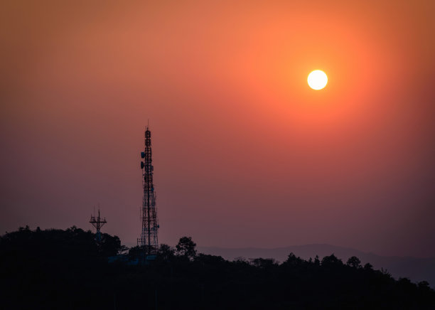 剪影电信天线塔的手机在山在日落背景。图片下载