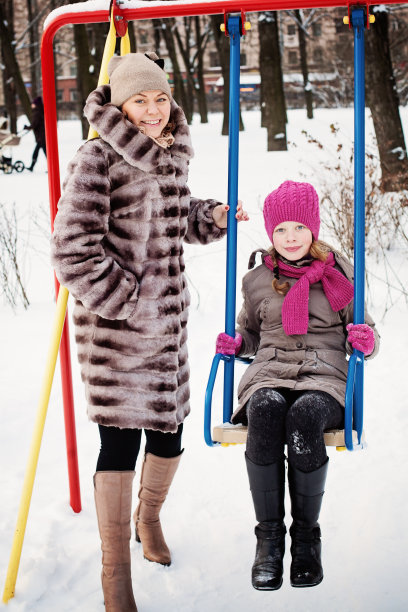冬天合家欢乐。母亲和女儿在户外荡秋千图片下载