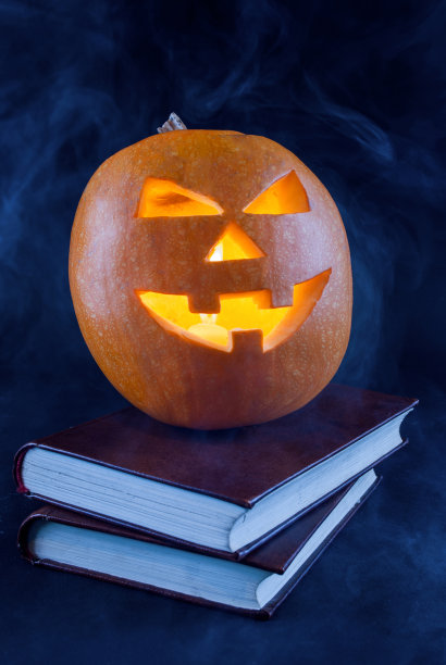 令人毛骨悚然的万圣节南瓜在旧书和烟熏和黑暗的背景图片下载