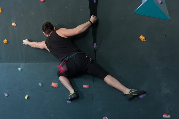 一个运动员在爬灰色的室内攀岩墙。图片下载