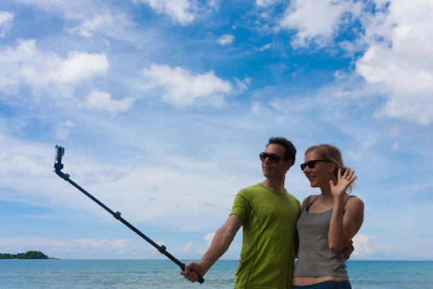 快乐的情侣在度假时用自拍杆和动作相机自拍照片或视频。图片下载