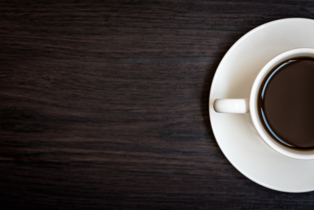 白色的咖啡杯在木桌背景与拷贝空间，半杯充满咖啡，暗色调的静物和小插画，俯视图为广告，商务和饮酒的概念，放松的概念图片下载