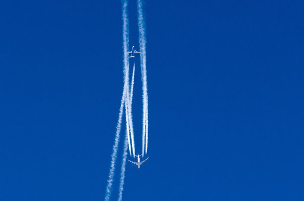 一架飞机在蓝天上穿过另一架飞机的航迹。图片下载