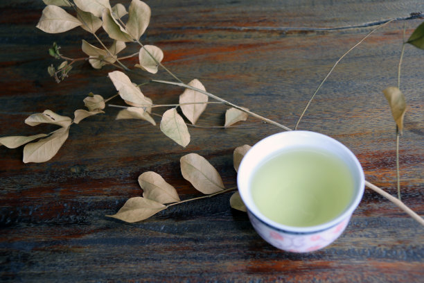 茶在杯与干枝叶，浅棕色的颜色在木桌上。图片下载