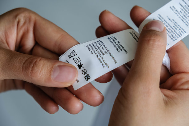 女人在看护理标签。有选择性的重点。女人的手拿着有清洁说明的衣服标签。阅读衣物标签显示洗涤说明的人丢失图片下载