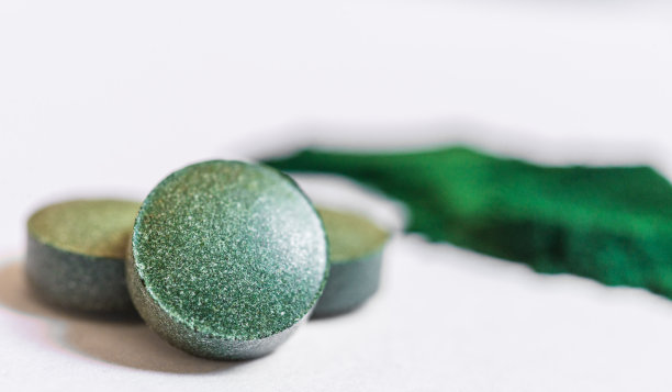 螺旋藻丸片微距照片，背景为白色。膳食补充剂、超级食品、健身和健康饮食理念。图片下载