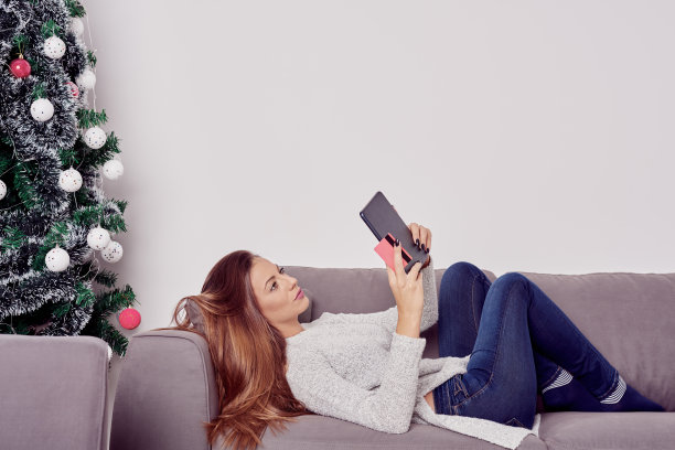 白种女人躺在沙发上，用平板电脑和圣诞节的概念图片下载