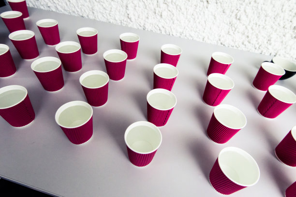 木桌上放着一排装水的一次性纸杯。会议、会议、试杯或拔杯期间的休息时间。图片下载