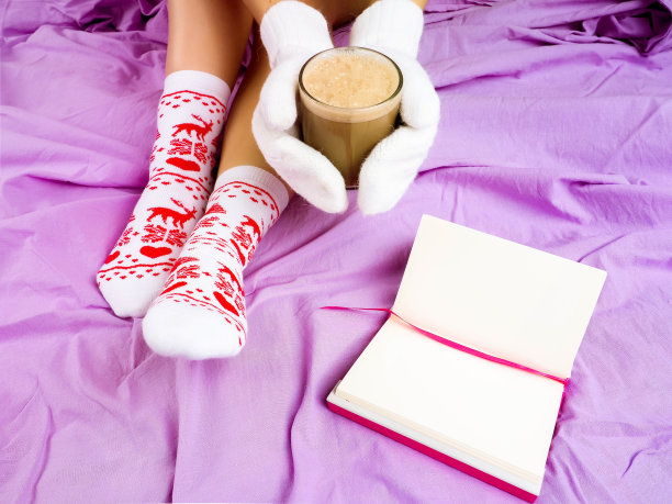 软照片的女人在床上的笔记本，一杯咖啡，顶部的观点。女人的腿在温暖的羊毛袜子。图片下载