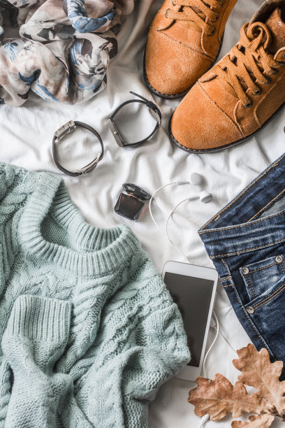 平铺女装秋走，俯视图。棕色麂皮靴子，牛仔裤，蓝色套头衫，围巾，手镯，手表，耳机，香水在灯光背景。时尚的概念素材图片