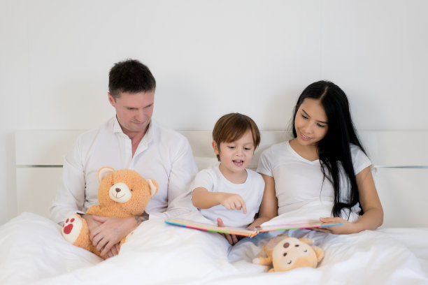 亚洲男孩和爸爸妈妈一起在卧室的床上看书。幸福的家庭的概念。图片下载