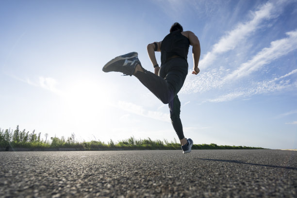 年轻的男运动员在柏油路上迎着天空奔跑图片下载