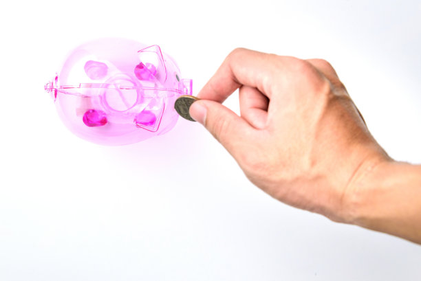 手扔硬币在粉红色小猪银行的白色背景上存钱的概念。图片下载