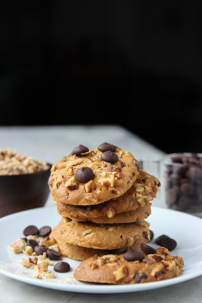 在黑色背景的白色盘子里，合上一堆巧克力片饼干。图片下载