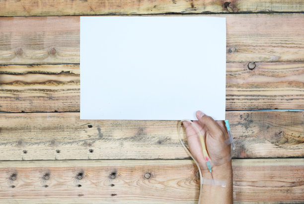 一名男子右手拿着生理盐水管，木桌背景上拿着一张纸图片下载