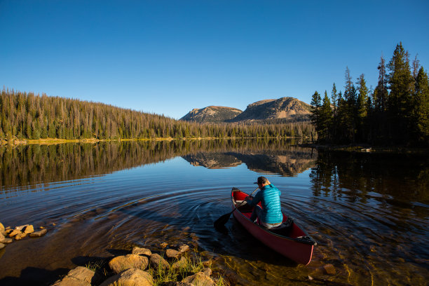 一名男子用桨将一只红色的独木舟划进湖中素材图片