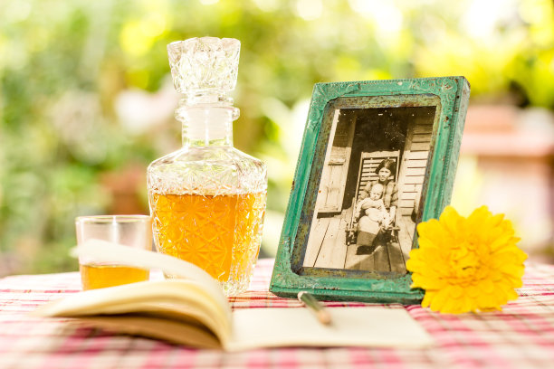 复古的绿色相框与老照片的母亲抱着她的儿子，放松的时间与笔记，日记和铅笔，威士忌在古董瓶和花园里的背景桌上黄色的花。温暖的家庭图片下载