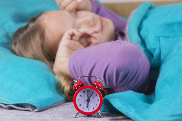 在床上的女孩从闹钟的声音醒来，伸伸懒腰从早上起床。图片下载