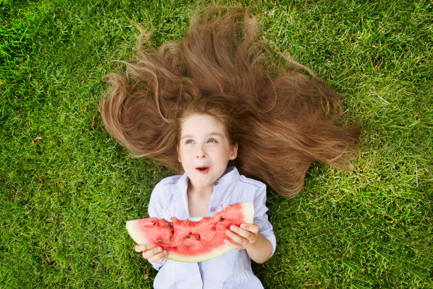 快乐可爱的小女孩躺在草地上吃西瓜在夏天的时间。快乐的小女孩在户外玩夏天。图片下载
