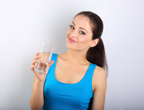 年轻美丽的女子饮用新鲜纯净的水从玻璃上的蓝色背景图片下载