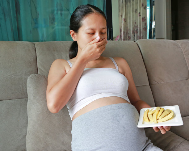 孕妇坐在沙发上，肚子上放着芒果脯。女人觉得恶心想吃酸水果。图片下载