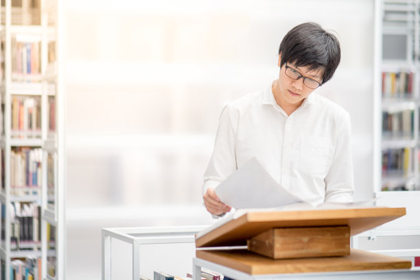 年轻的亚洲男大学生在图书馆的讲台上阅读推荐书籍素材图片