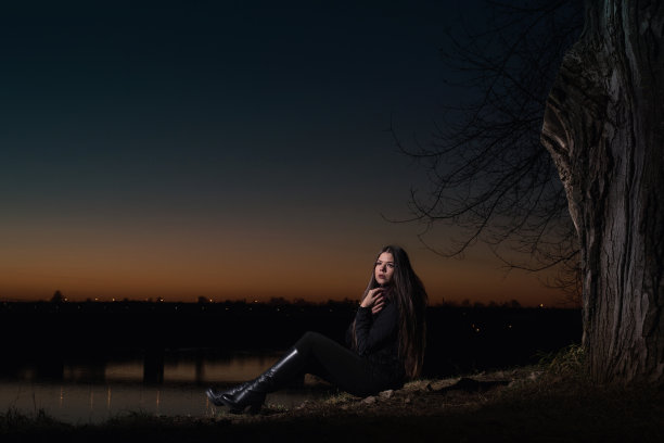 晚上，一个女孩坐在一棵大树下。背景是一座横跨河上的桥图片下载