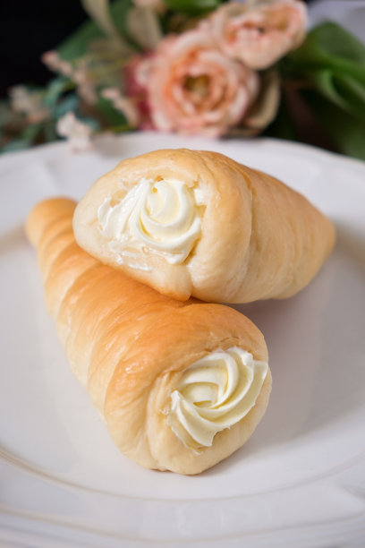 两个奶油角，带白色奶油馅的糕点角，木桌背景上的白色盘子上的奶油蛋卷。图片下载