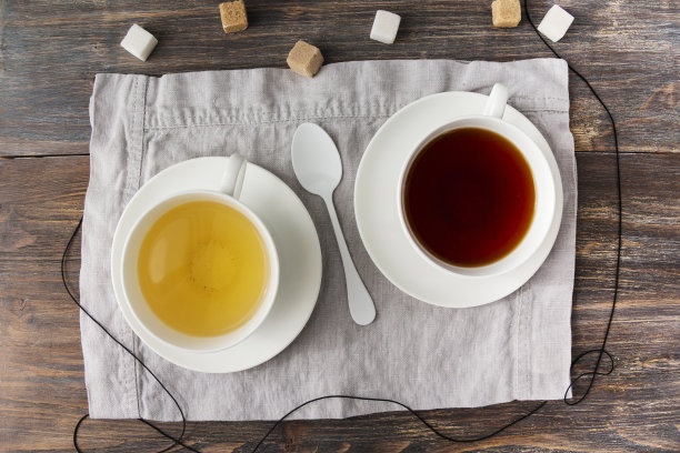 两杯红茶和绿茶，甘蔗和白方糖放在木桌上。前视图。素材图片