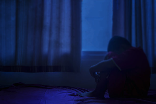 模糊沮丧的男人双手抱头坐在黑暗的卧室的床上。图片下载