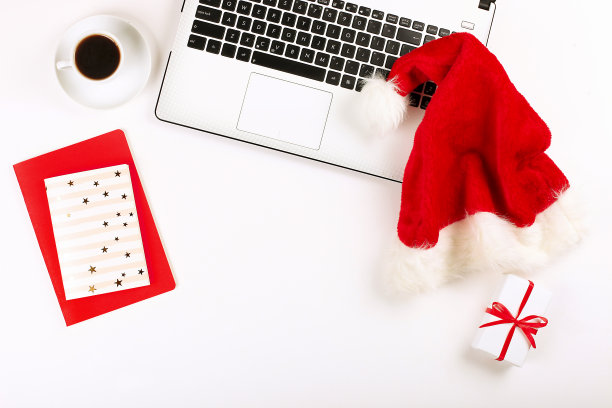 办公桌上放着咖啡，笔记本电脑，圣诞礼物和圣诞帽在白色的背景平与复印空间图片下载