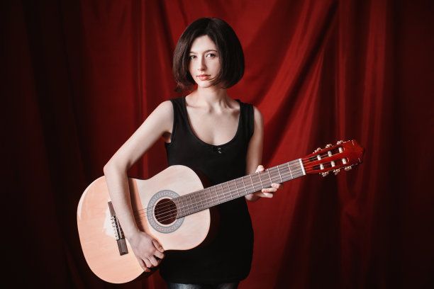 情绪肖像的黑发女孩与短直黑发自然化妆在一个红色的背景。一个穿着黑色t恤手里拿着吉他的女人图片下载