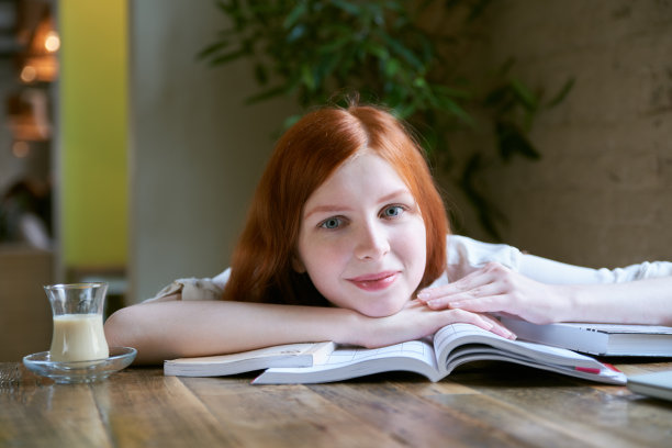 年轻迷人的微笑的女学生的肖像与长红头发和微笑在我的脸上。一个愉快的阅读，休息和学习的概念图片下载