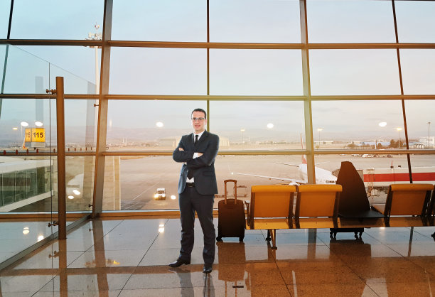 一个商人站在机场的窗口前，一架飞机正在靠近图片下载