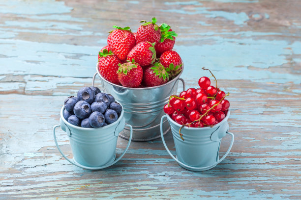 浆果装在三个蓝色的罐子里，放在蓝色的旧木桌上图片下载