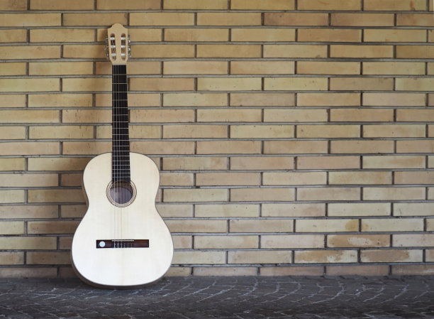 在斑岩人行道上，靠在一堵旧砖墙上的原声吉他图片下载