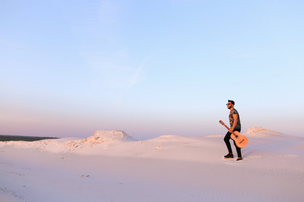 穆斯林青年拿着吉他在沙漠中行走图片下载