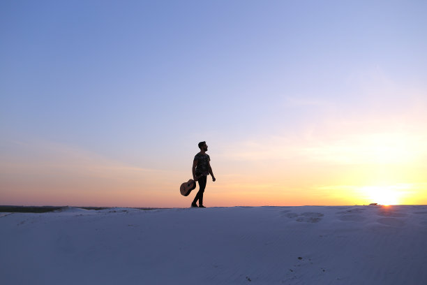 阿拉伯男子在沙丘上手持吉他行走图片下载