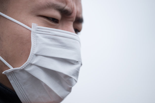 一个年轻的亚洲人戴着白色面具站在雾天里素材图片