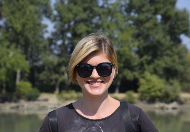 年轻美丽的女孩戴着太阳镜，背景是河的风景，画像的金发。图片下载