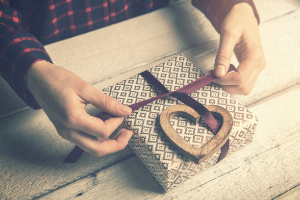 女人给心爱的人包装礼物。用木制的心形装饰系一个丝带蝴蝶结图片下载