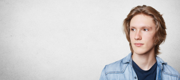 照片中，一位穿着牛仔衬衫、神情沉思的时尚男士正在考虑未来的计划。时尚男学生梦想假期，在白色混凝土墙上摆姿势，复制空间图片下载