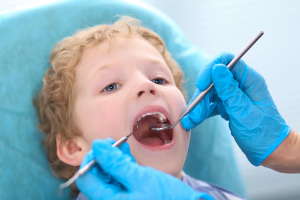 小卷毛男孩在牙科医生检查口腔时张大了嘴巴。图片下载