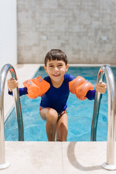 可爱的小男孩穿着泳衣，手臂浮在游泳池里图片下载