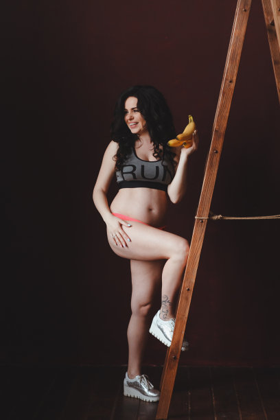 年轻孕妇看起来很健康，在阁楼工作室的梯子上拿着香蕉图片下载