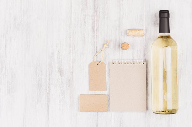 空白米色牛皮纸包装，文具，商品与瓶白葡萄酒在柔软的白色木材背景，复制空间。图片下载
