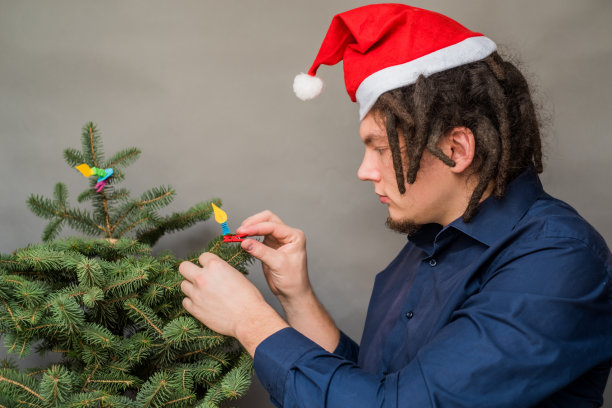 高加索男子的非洲发型和圣诞帽挂在圣诞树上的装饰品图片下载