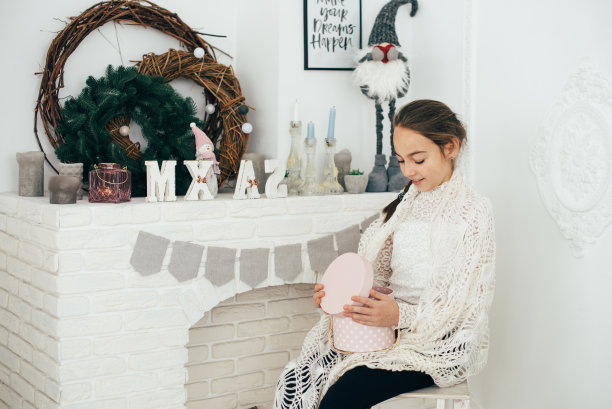 那个女孩围着一条织好的白围巾坐在壁炉边。图片下载