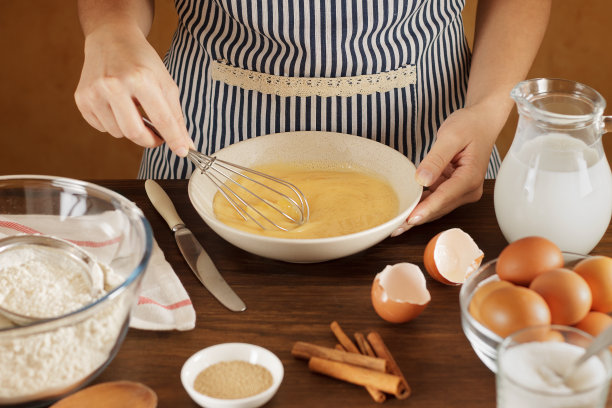 一名妇女在厨房的陶瓷碗里搅拌鸡蛋和牛奶。图片下载